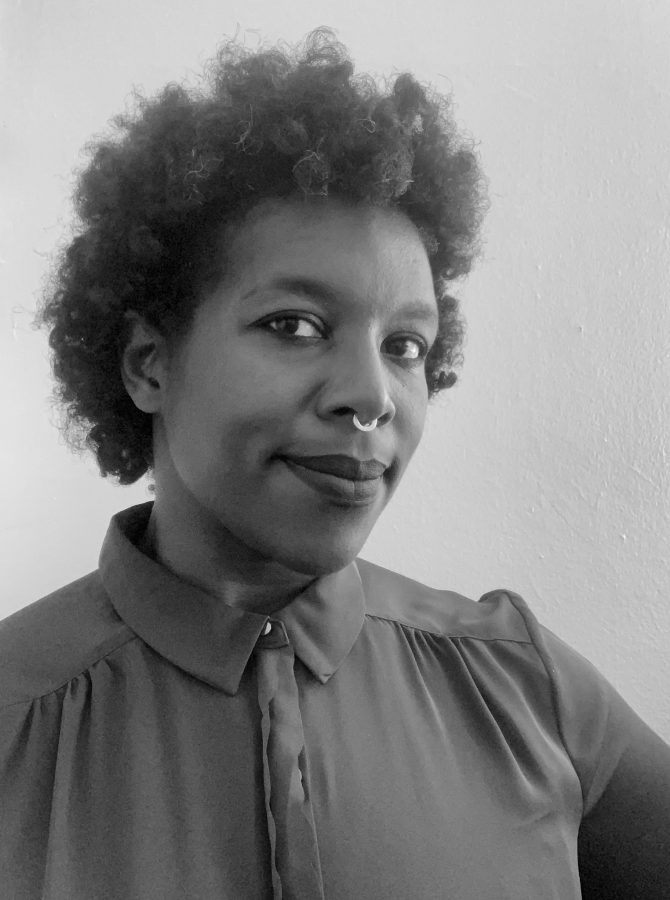 A greyscale image of Brittney Frantece, a Black woman. She's wearing a dark button down shirt and has her septum pierced. You can see her thick curly hair, surrounding her face; it is not long enough to reach her shoulders. 
