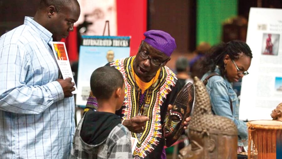 Mr. Delbert Richardson, holding an African mask as he talks to a young Black boy and his guardian. 